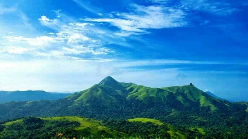 A panoramic view of mist-covered Western Ghats mountains and lush green forests.