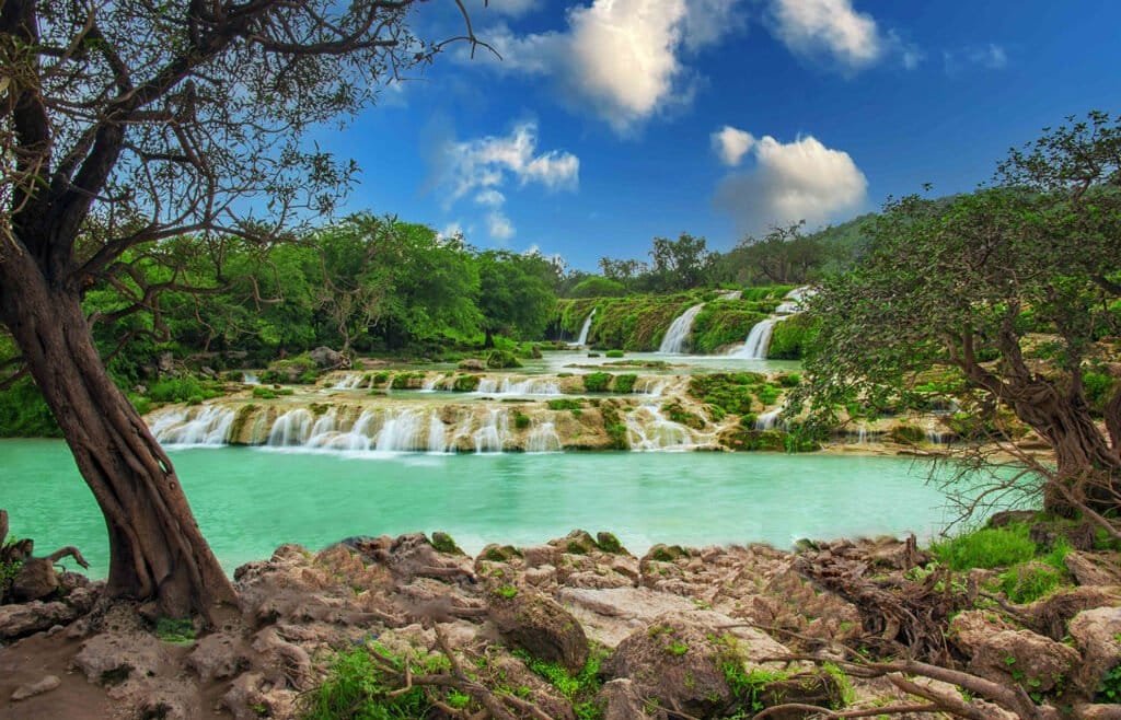 A lush green landscape in Salalah, Oman, during the Khareef season, with misty mountains, verdant valleys, and a serene coastline.