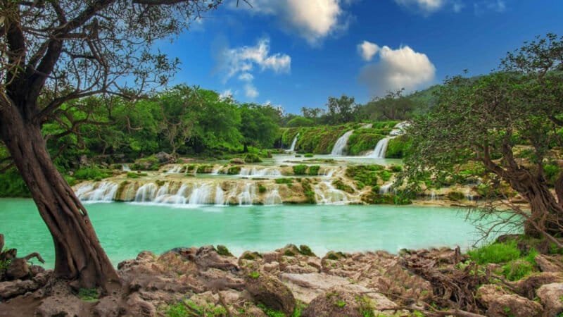 A lush green landscape in Salalah, Oman, during the Khareef season, with misty mountains, verdant valleys, and a serene coastline.
