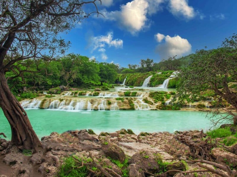 A lush green landscape in Salalah, Oman, during the Khareef season, with misty mountains, verdant valleys, and a serene coastline.