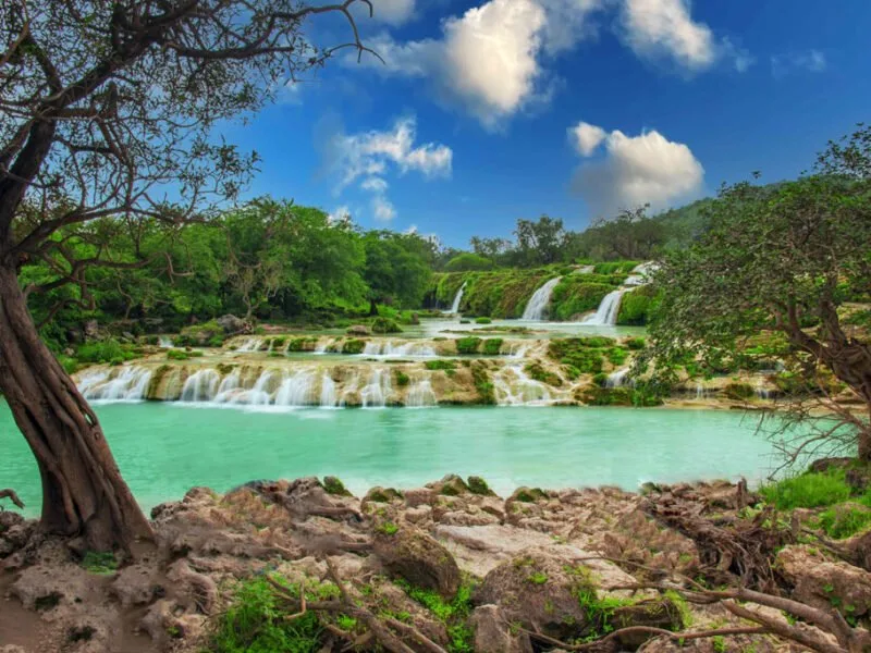 A lush green landscape in Salalah, Oman, during the Khareef season, with misty mountains, verdant valleys, and a serene coastline.